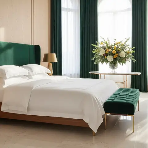 A bedroom with a tufted emerald headboard, crisp white linens and a matching velvet bench